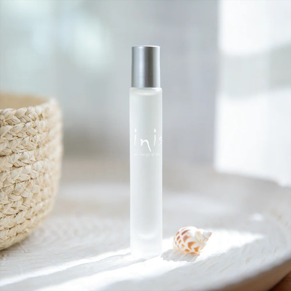 Inis roll-on fragrance frosted bottle on white dish with seashell, beside a wicker basket in natural light