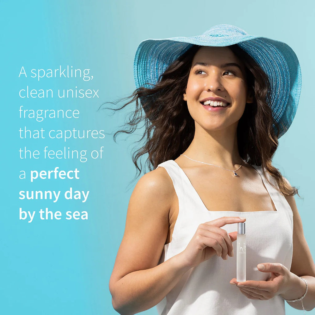 Smiling woman in blue sun hat holding Inis roll-on with text: A sparkling, clean unisex fragrance that captures the feeling of a perfect sunny day by the sea