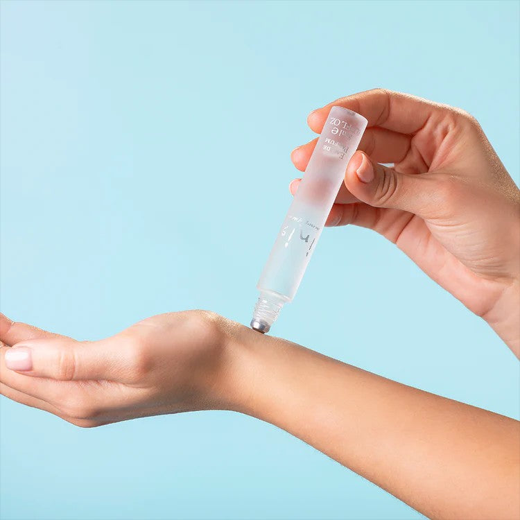 Hands applying Inis roll-on fragrance to inner wrist on blue background